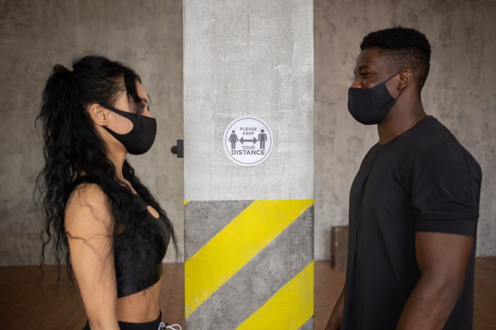 Crafting Captivating Headlines: Your awesome post title goes here Two people practicing social distancing with masks indoors near a safety sign.
