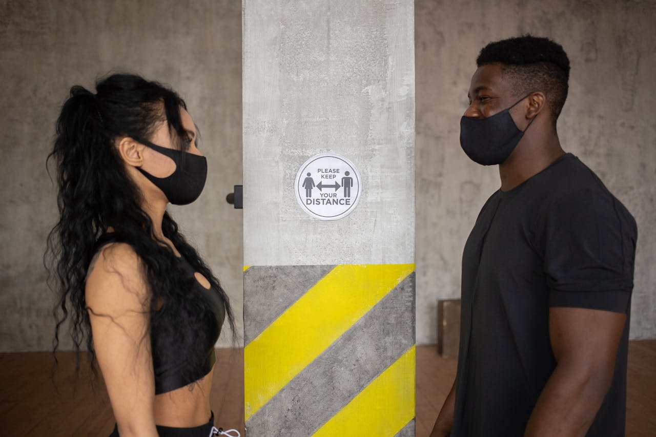 Crafting Captivating Headlines: Your awesome post title goes here Two people practicing social distancing with masks indoors near a safety sign.